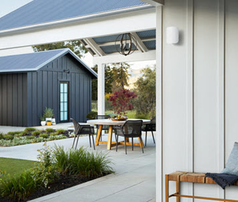 A view of a backyard patio with an eero Outdoor 7 device on the side of a house.